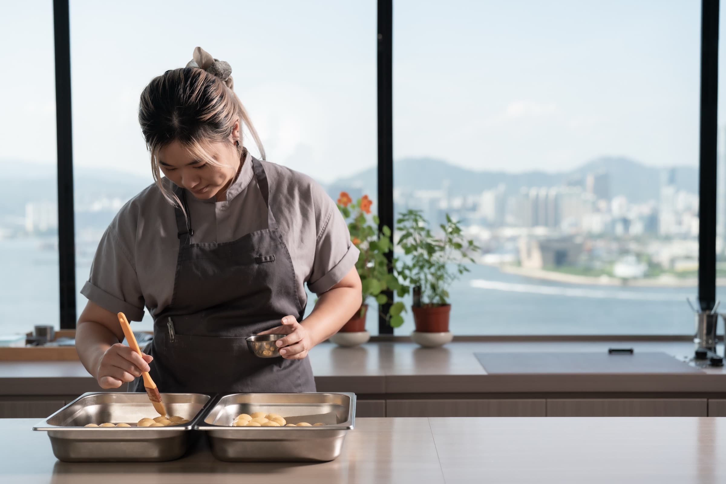 A chef at æra glazing pastries with the Hong Kong harbour skyline in the background