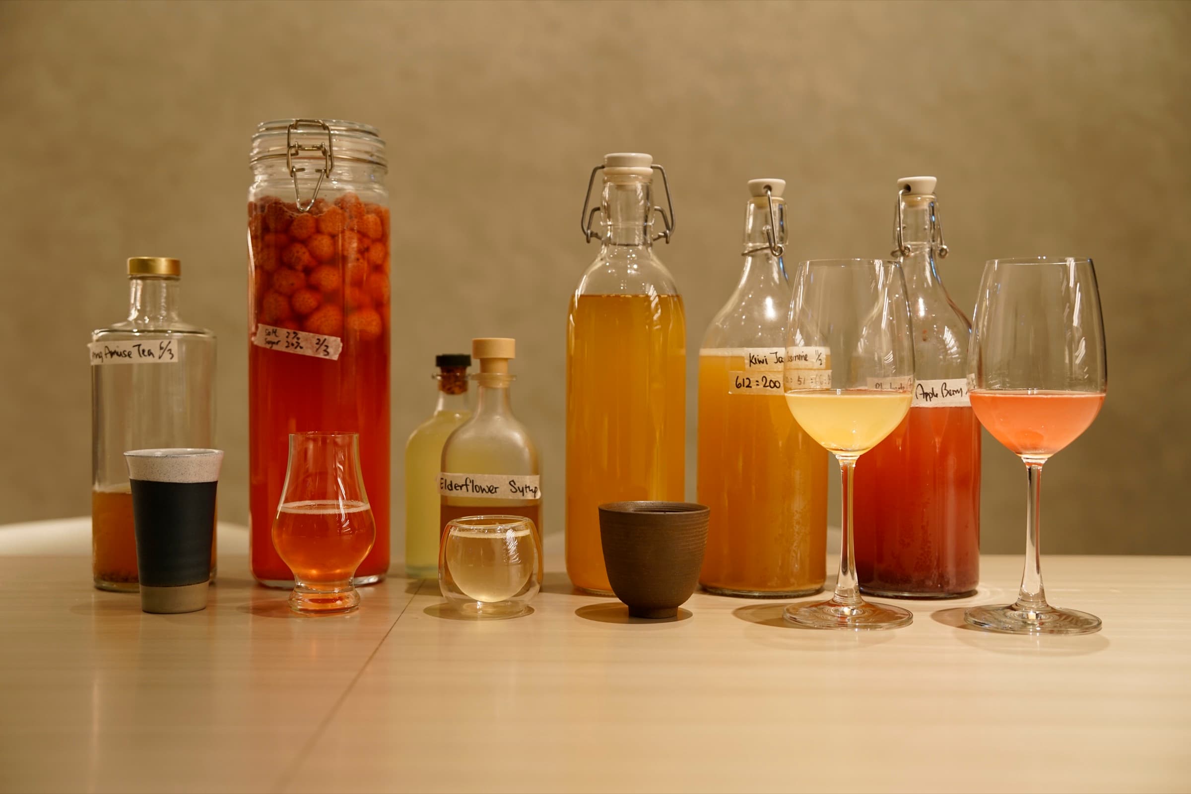 A lineup of house-made non-alcoholic pairings — rose jasmine tea, elderflower syrup, kiwi jasmine, and rhubarb-apple cordial — bottled, labeled, and poured into glasses.
